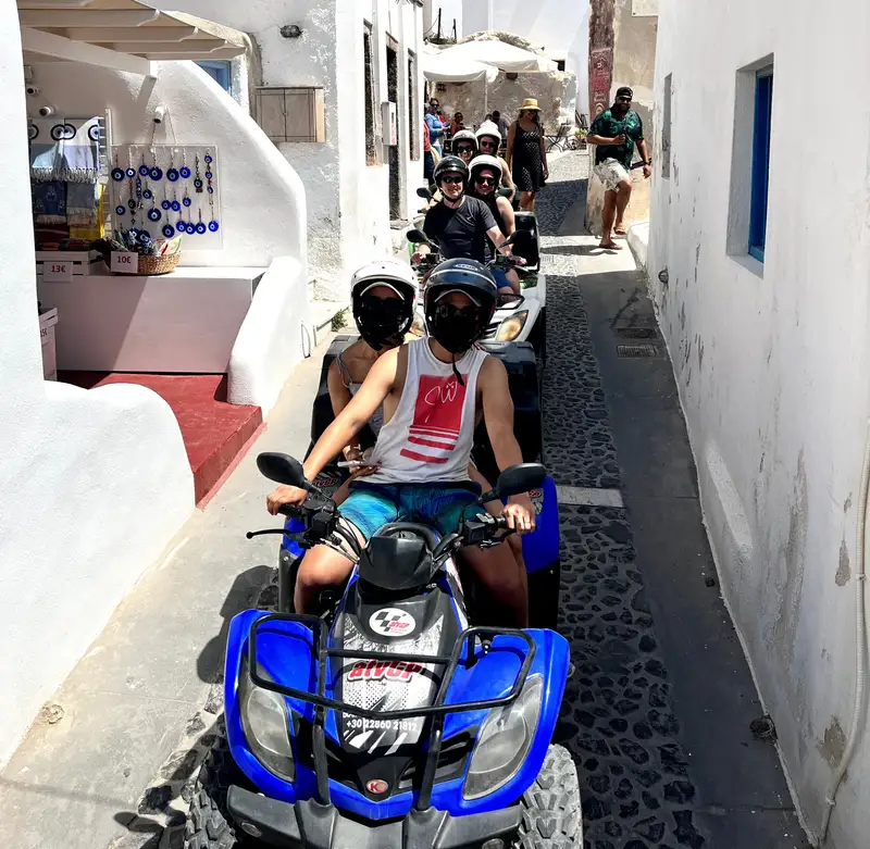 Quad bikes riding through a narrow whitewashed Santorini village lane